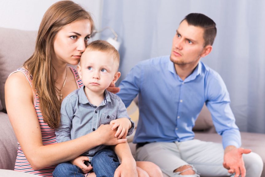 wife holding a child while her husband is upset with her, couple considering getting a divorce